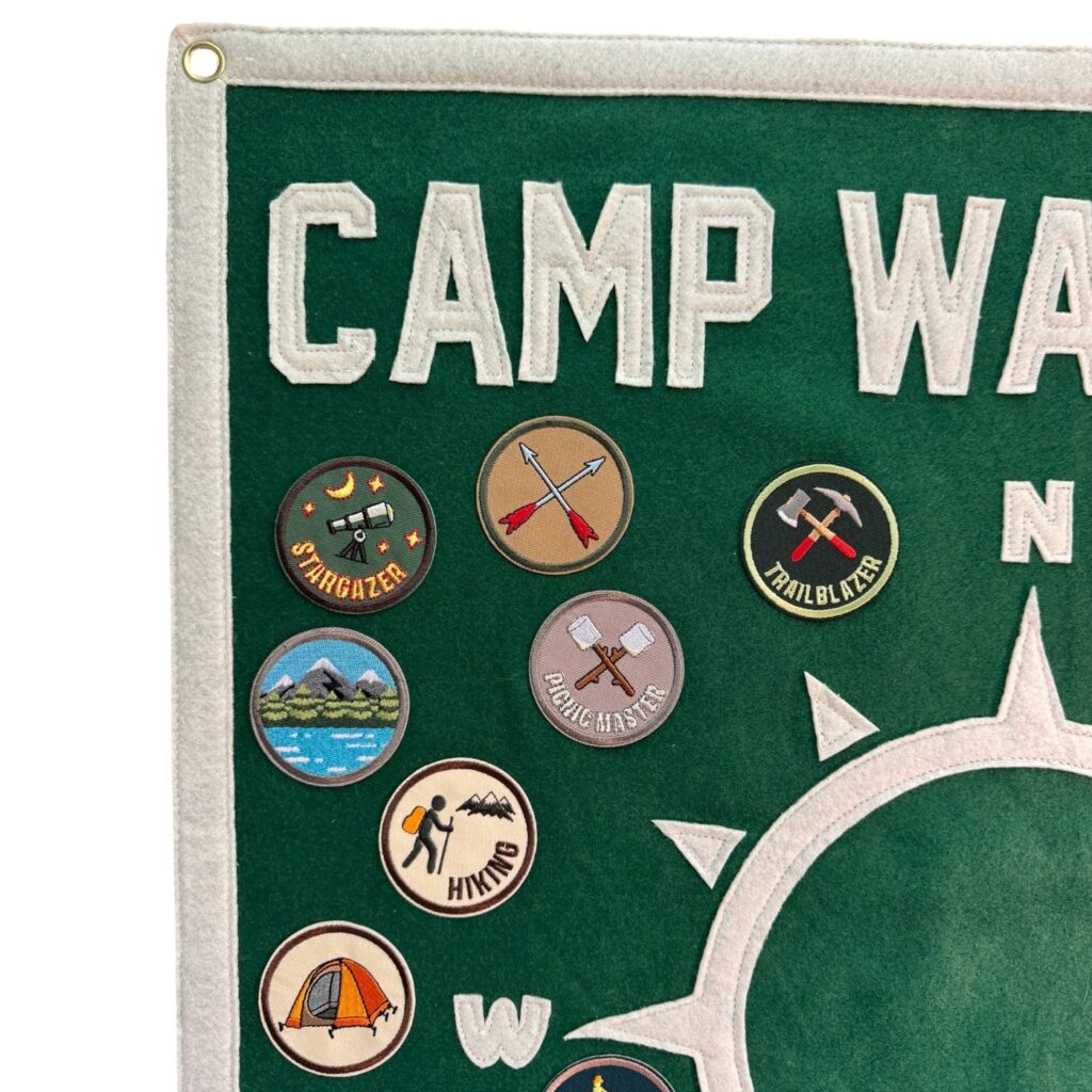 Close-up of Camp Wayfarer lettering and embroidered patches including stargazer, trailblazer and hiking
