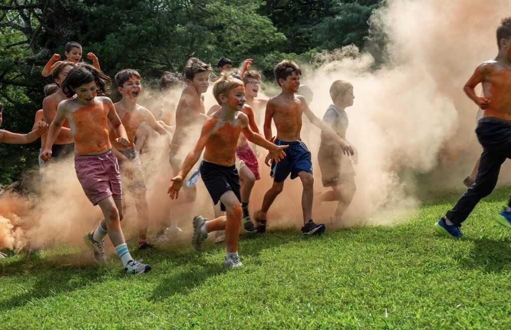 Campers running across a grassy field through clouds of orange color smoke at Color War