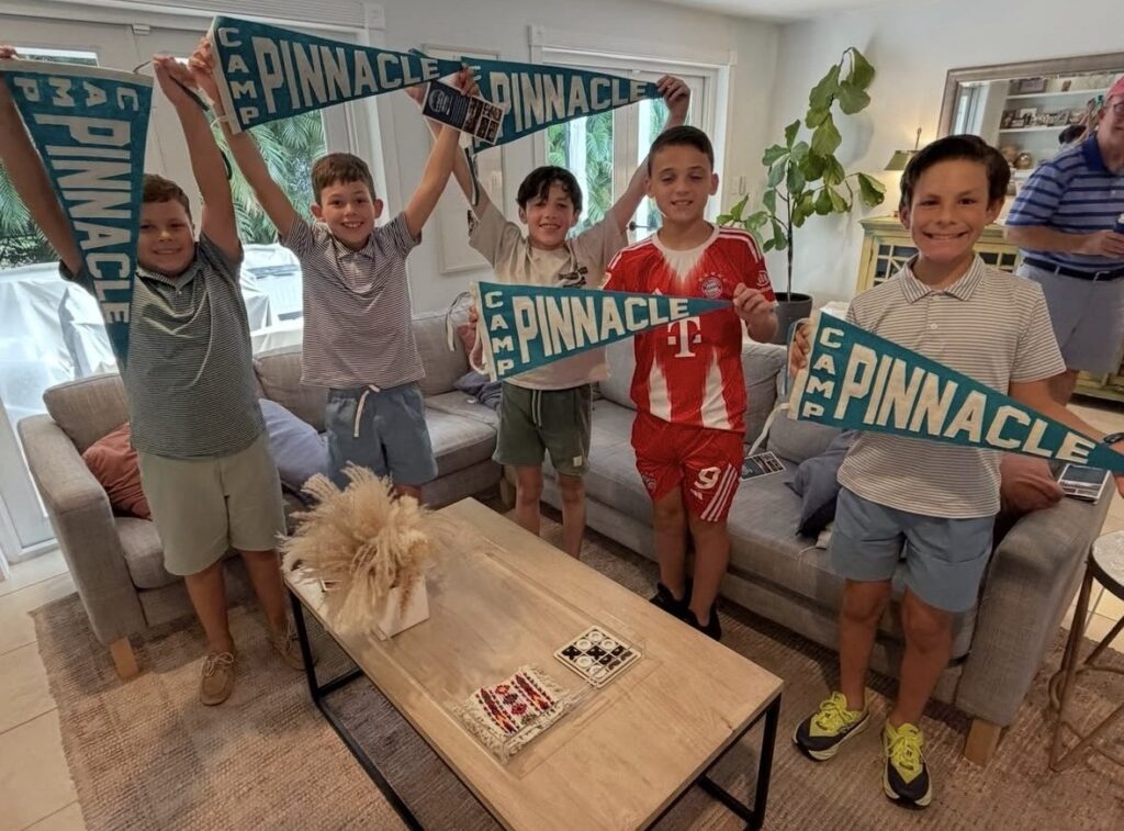 Smiling kids in a living room holding up Camp Pinnacle felt pennants