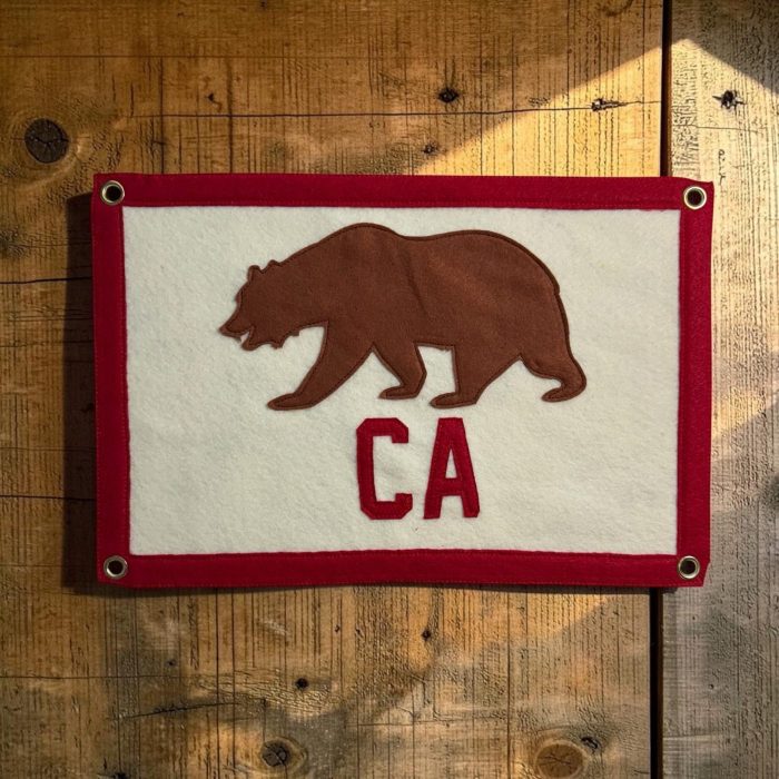 White felt banner with red trim, a brown felt bear and CA lettering hanging on a wood wall