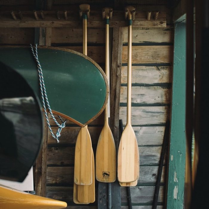 Wooden canoe paddles and a green canoe hanging in a camp boathouse