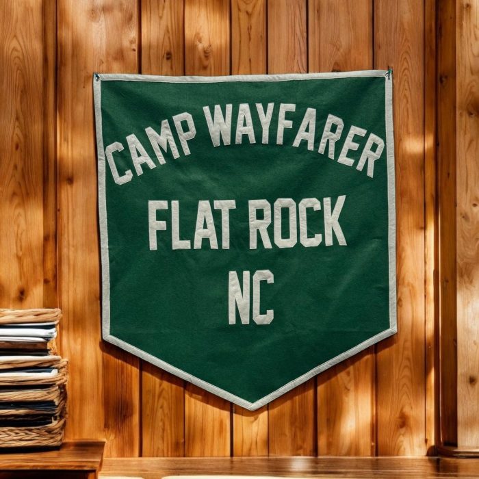 Green felt camp banner reading Camp Wayfarer Flat Rock NC hanging on a warm wood cabin wall