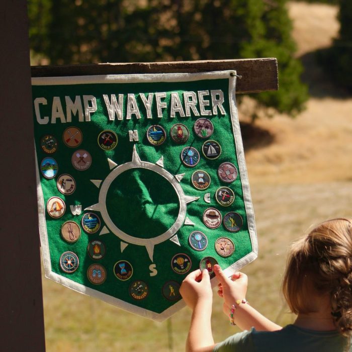 Camper pinning an award patch onto a green Camp Wayfarer compass pennant outdoors