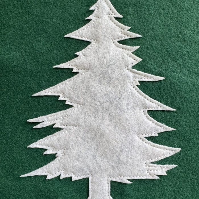 Close-up of a cream felt pine tree applique with visible stitching on green wool felt