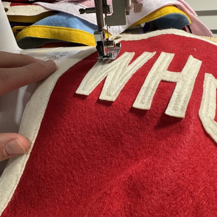 Felt lettering being stitched onto a red custom camp pennant at a sewing machine with colorful felt behind it