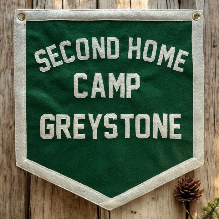 Green felt banner reading Second Home Camp Greystone on a wood post with pine cones