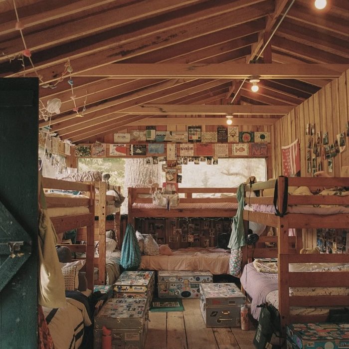 Inside a summer camp cabin with wooden bunk beds, trunks and memorabilia on the walls