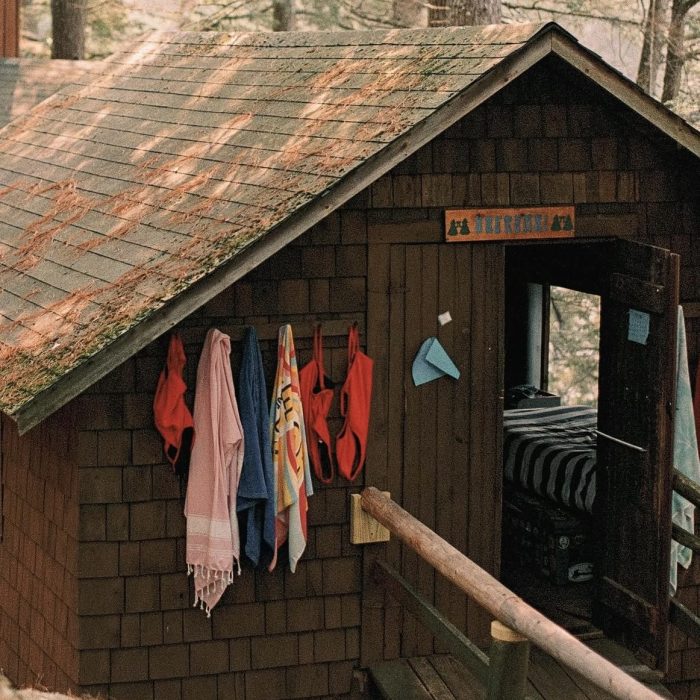 Brown shingled summer camp cabin with colorful towels hanging on hooks beside the porch