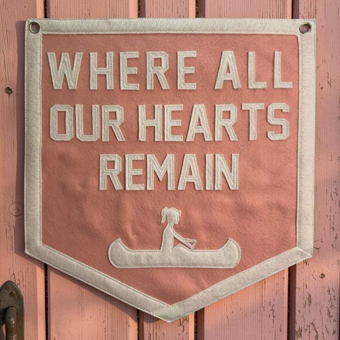 Coral felt camp banner reading Where All Our Hearts Remain with a cream felt canoe design