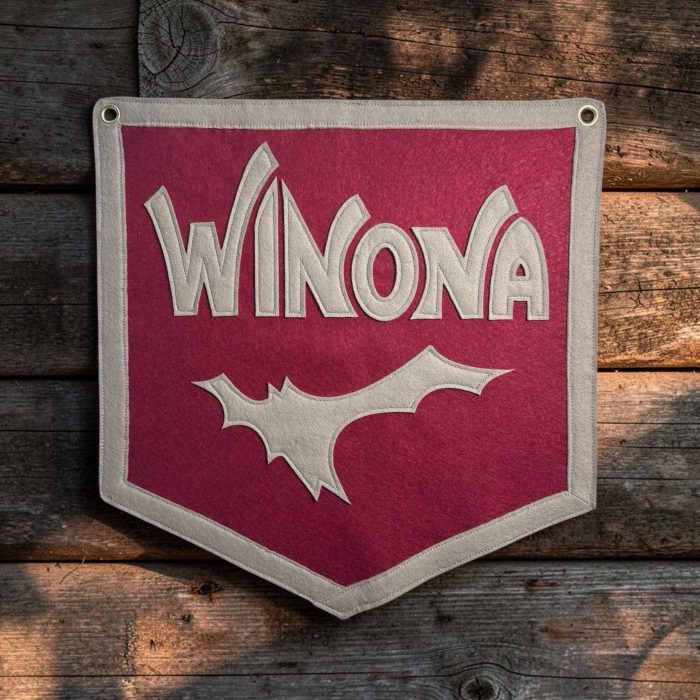 Magenta felt camp banner with cream felt Winona lettering hanging on a rustic wood wall